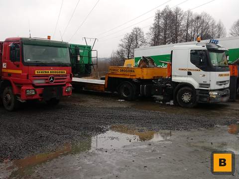 Ciągnik siodłowy z pustą naczepą niskopodwoziową i łyżką koparkową na placu w Częstochowie