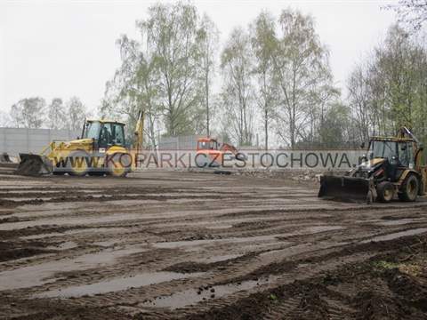 Dwie koparko-ładowarki równają duży plac przy betonowym ogrodzeniu w Częstochowie